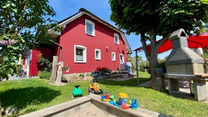 Ein rotes Haus mit einem Steinofen, ein kleiner Garten mit Spielzeug und einem roten Zaun.