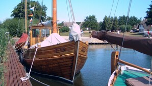Ein hölzernes Boot liegt an einem Steg, mit einem überdachten Kämmerchen und einer Flagge.
