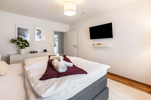 Una camera d'albergo moderna con un letto, una TV a parete e una pianta sul comodino.