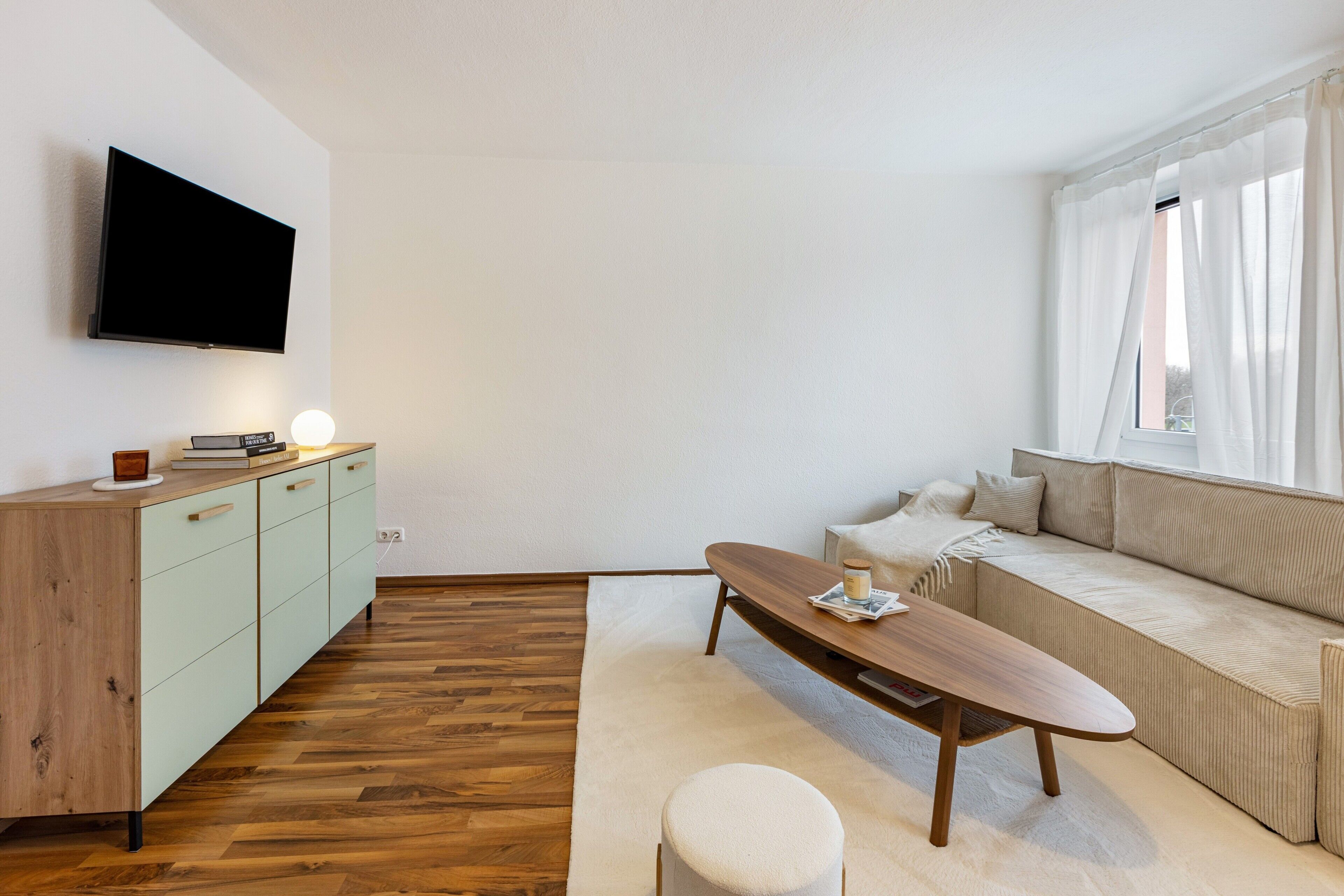 Un salon moderne avec un téléviseur à écran plat, une table basse en bois, un canapé et un tapis de couleur claire.