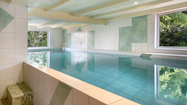 Una piscina interior con vistas a árboles a través de amplias ventanas.