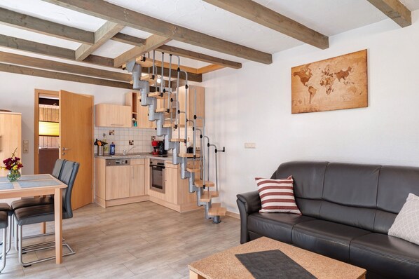 Une cuisine moderne avec un escalier intégré, un coin repas avec une table et des chaises, et un salon avec un canapé et des coussins.