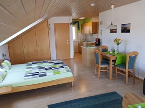 A bedroom with a bed, a dining table with chairs, a kitchen area, and a small island with a coffee maker.