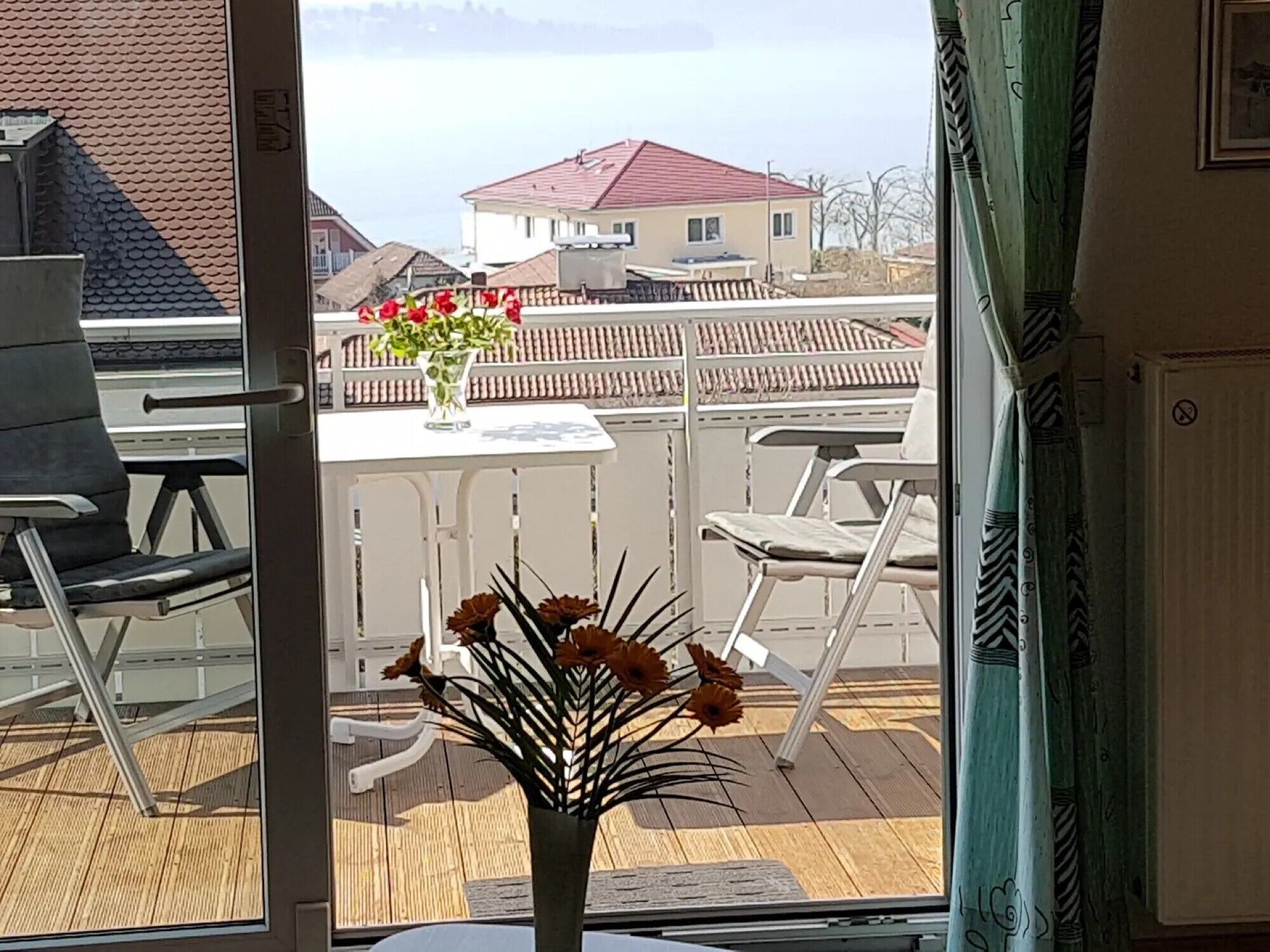 Uma varanda com móveis de exterior, uma mesa e um vaso de flores.