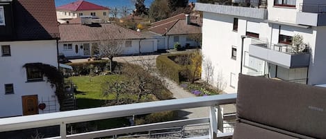 A balcony with a view of a lake, adjacent buildings, and a garden.