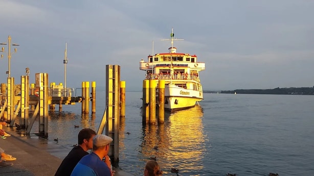 Un ferry amarrado en un muelle, con vista despejada al agua y a la costa distante.