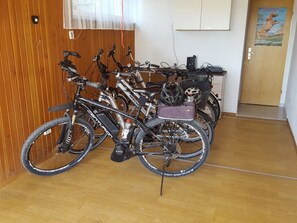 A room with wooden flooring, a wall-mounted electrical outlet, a door with a poster, and a bicycle rack with multiple bicycles.