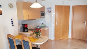 Una cocina compacta con armarios de madera, cafetera, lavamanos y un comedor con sillas.