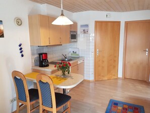 A compact kitchen with wooden cabinets, a coffee maker, a sink, and a dining area with chairs.