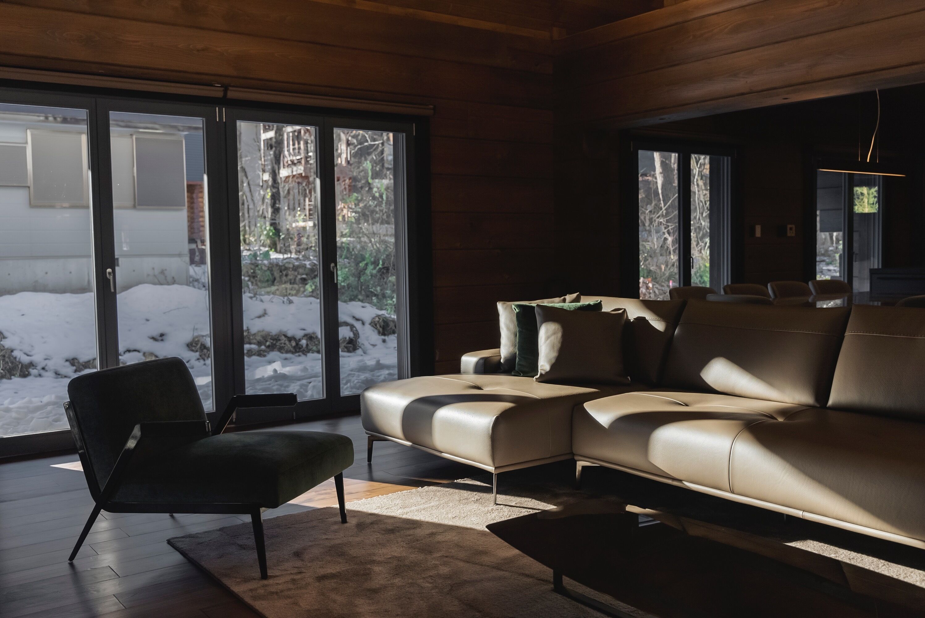 A modern living room with a leather sofa, a black armchair, and a large window with a view of a snowy outdoor area.