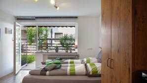 Ein Schlafzimmer mit einem Bett, einem Holzschrank, einem Fenster mit Blick auf Grünflächen und einer Deckenleuchte.