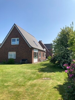 Une maison en briques avec un toit en pente, un porche à l’avant et une pelouse bien entretenue.