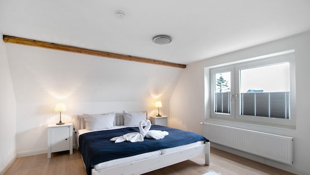 A bedroom with a bed, two bedside tables, a window, and a radiator. - Holiday Home 'Haushälfte Am Süderhafen' with Private Terrace, Private Garden and Wi-Fi (Nordstrand)