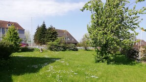 A grassy yard with a tree, a fence, and a house in the background. - Holiday Home 'Haushälfte Am Süderhafen' with Private Terrace, Private Garden and Wi-Fi (Nordstrand)