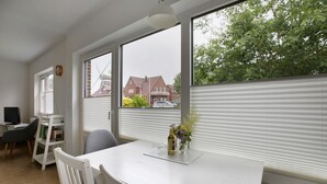 A room with a white table, a chair, a bookshelf, a desk with a computer, and a window with blinds. - Holiday Home 'Haushälfte Am Süderhafen' with Private Terrace, Private Garden and Wi-Fi (Nordstrand)