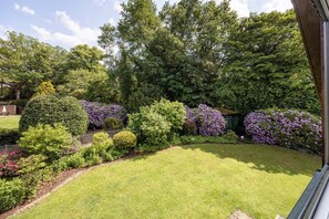 Un jardin bien entretenu, agrémenté de divers arbustes et arbres, une pelouse soigneusement taillée et un chemin pavé de briques.