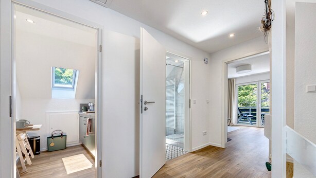A modern interior with a wooden floor, a kitchen area, and a bathroom visible through an open door. - Apartment with Balcony and Wi-Fi (Lüneburg)