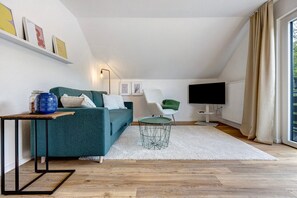 Un salon moderne avec un canapé, une table basse ronde, un téléviseur et une grande fenêtre avec des rideaux.