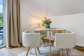A room with a round table, four chairs, a lamp, a vase with plants, and a window with curtains.
