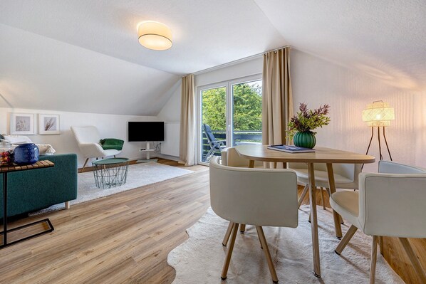 Un salon moderne comprenant un canapé, une table à manger, des chaises, un téléviseur et une grande fenêtre.