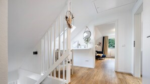 A modern interior with a wooden staircase, white walls, and a view into a living area with a sofa and curtains. - Apartment with Balcony and Wi-Fi (Lüneburg)