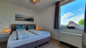 A bedroom with a bed, bedside lamps, a painting, a window with a view of a boat, and a ceiling light fixture. - Apartment 'Penthouse Laboe' with Sea View, Private Terrace and Wi-Fi (Laboe)