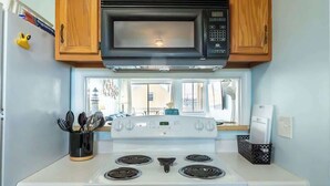 Una cocina con armarios de madera, microondas, estufa y ventana con vista a edificios.