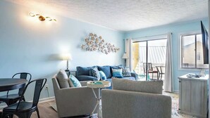 Una sala de estar con pared azul, un sofá, dos sillones, una mesa de comedor con sillas, una lámpara y un adorno de pared.