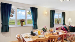 A dining area with a table set for breakfast, two chairs, a floral sofa, and a view of the outdoors through the windows.