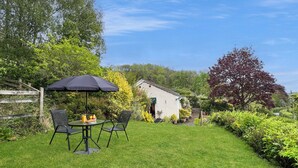A grassy backyard with a table and chairs, a wooden fence, and a house in the background.