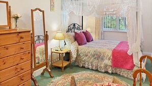 A bedroom with a canopy bed, a bedside table with a lamp, a dresser, and a mirror.