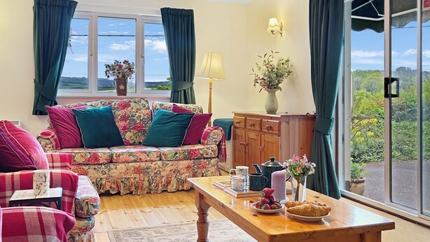 A living room with a sofa, chairs, a table with food, and a view through a large window.