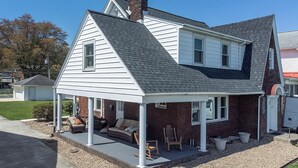 A two-story house with a covered porch, a brick chimney, and a small garden area with outdoor furniture. - River House - Harrisburg City Skyline Views with Game Room and Covered Porch (Wormleysburg)