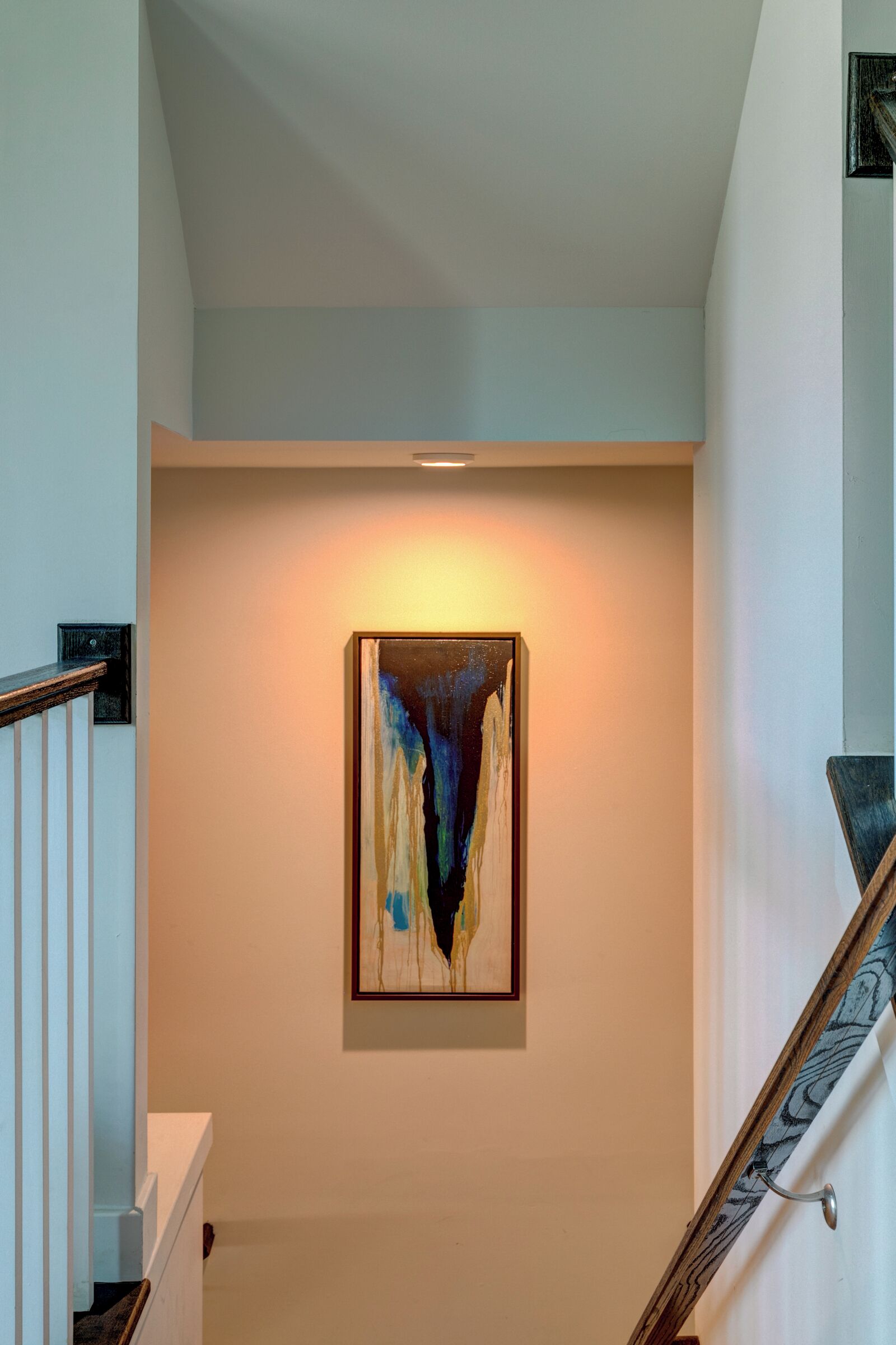 Una escalera de diseño moderno, un cuadro abstracto enmarcado en la pared y una barandilla de madera.