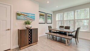 Uma área de refeições com mesa e cadeiras de madeira, um armário com uma planta e quadros na parede.