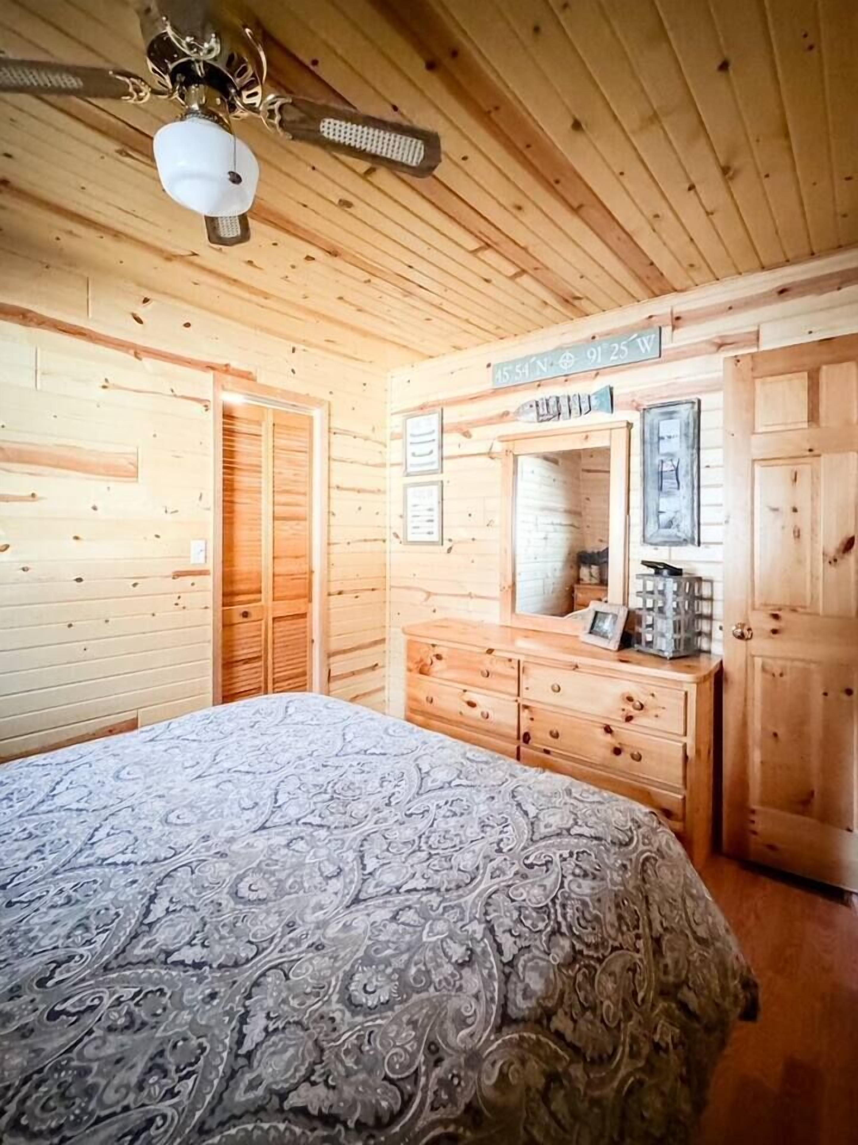 A wooden cabin bedroom with a bed, dresser, and mirror.