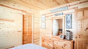A wooden cabin bedroom with a bed, dresser, and mirror.