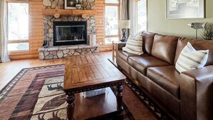 A log cabin interior with a stone fireplace, leather sofa, and a wooden coffee table. - Lakefront Cabin on LCO - The Sunset Escape (Hayward)