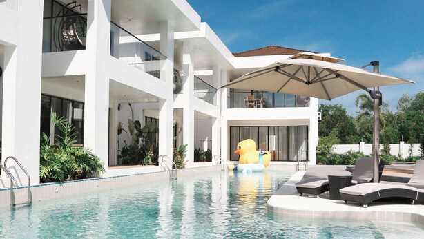 Un hotel moderno con piscina, asientos al aire libre y un amplio paraguas.
