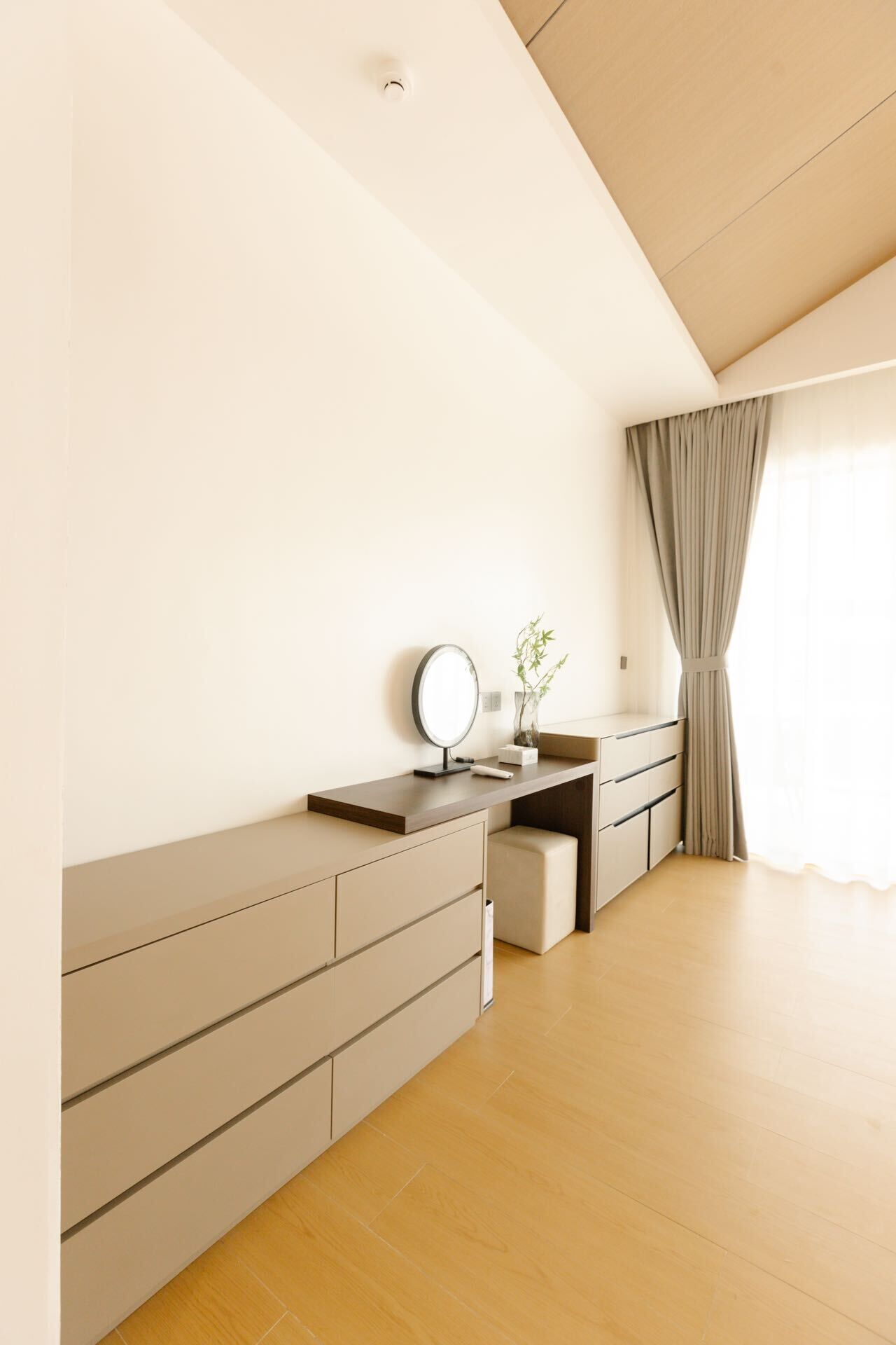 Un dormitorio moderno con suelo de madera, un escritorio empotrado con espejo y una mesita de noche con un florero.