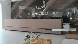 Zona de recepción con diseño moderno, que incluye un mostrador de recepción,  área de descanso y un amplio ventanal con el nombre "WILLANDER RESORT".