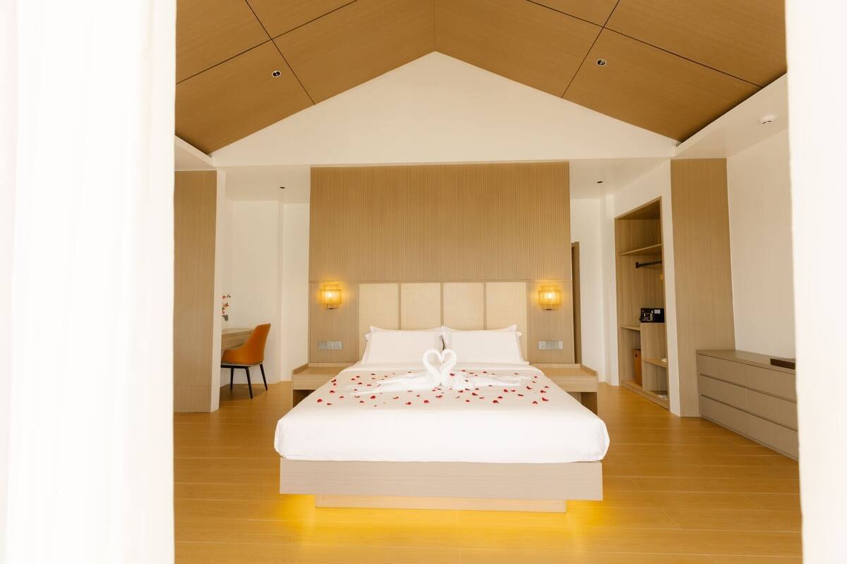 A modern hotel room with a large bed, a desk, and a wardrobe.