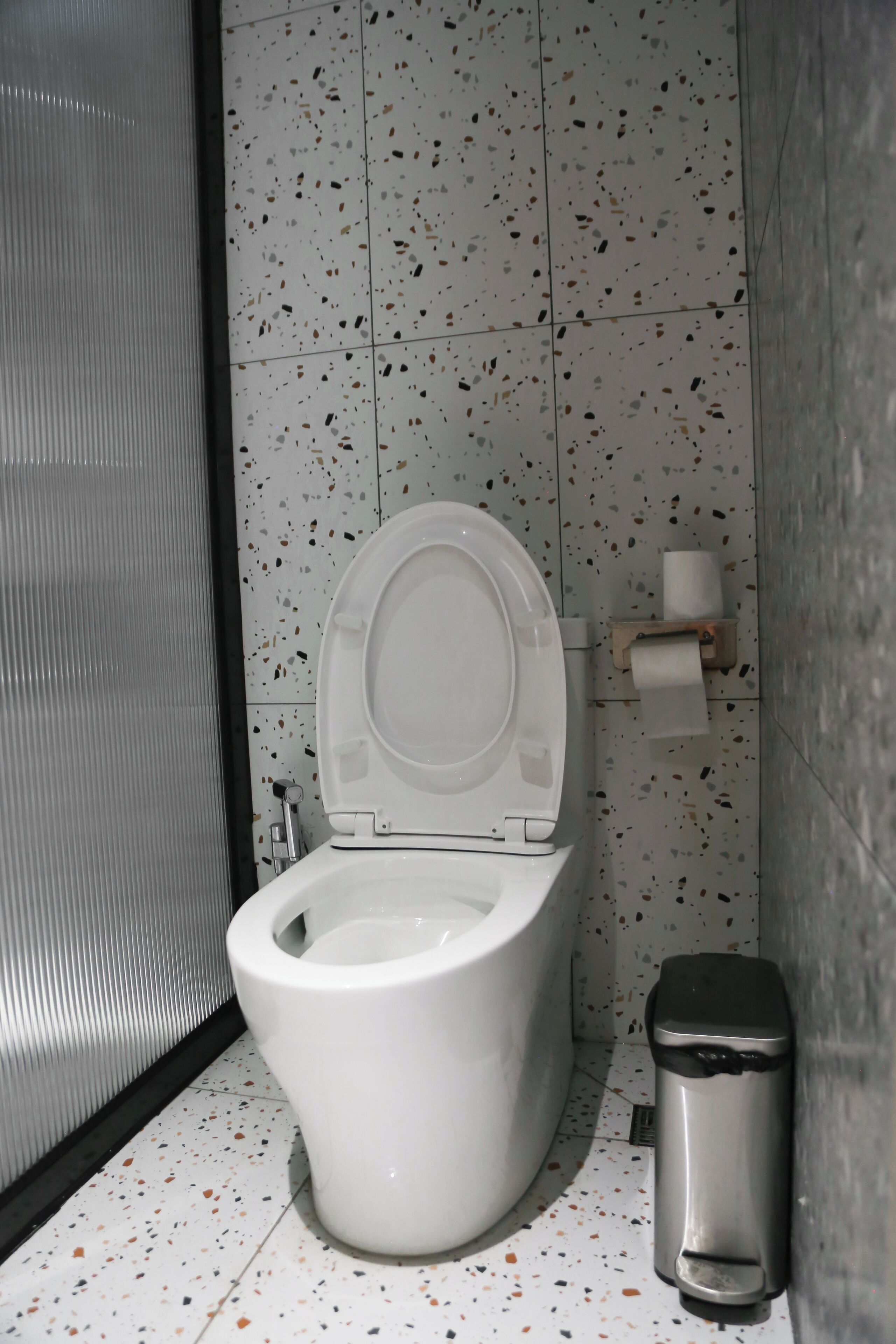 A modern bathroom with a white toilet, a trash bin, and a paper towel dispenser.