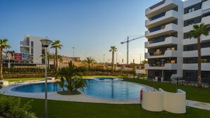 A modern building with a swimming pool surrounded by palm trees and a well-maintained lawn.
