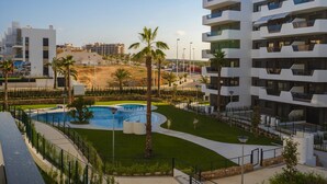 A modern hotel with a swimming pool, palm trees, and a well-maintained lawn.