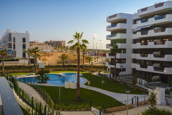 A modern hotel with a swimming pool, palm trees, and a well-maintained lawn.