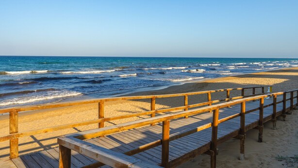 A wooden boardwalk leading to a sandy beach with the ocean in the background.