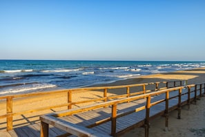 A wooden boardwalk leading to a sandy beach with the ocean in the background.