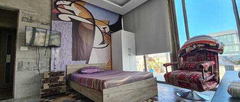 A modern bedroom with a bed, a large abstract mural, a television, and a British flag-patterned chair.