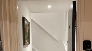 Un pasillo que lleva a una escalera con alfombra a rayas y un cuadro en la pared.